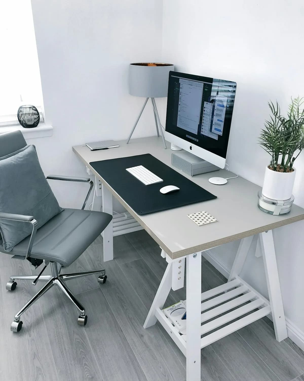 A calm home office with a pale desk, task lamp and plants