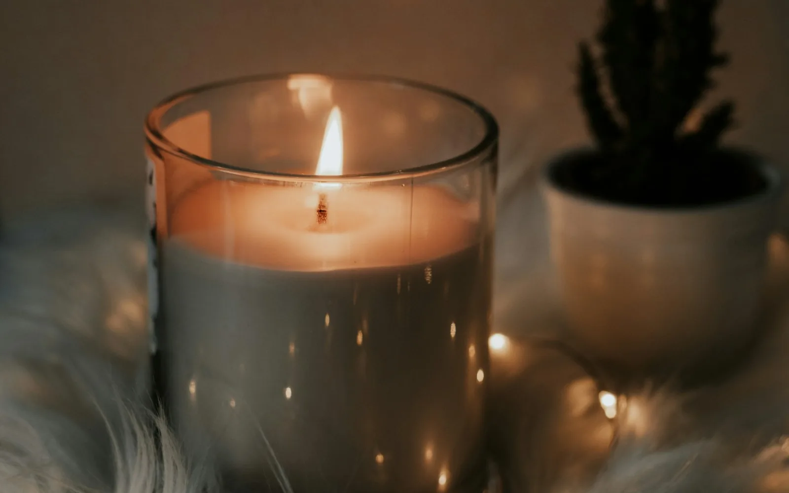 A lit candle in an amber glass vessel beside a plant